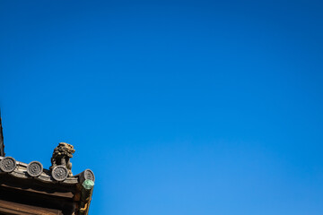 A Komainu, or lion, standing watch on the corner of a traditional Japanese structure against a blue sky