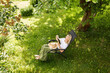 © Girts - Woman reading a book in garden recliner chair. Summer vacation in the yard. Mature Scandinavian female life in retirement. Good living. View from the top. Beautiful middle aged woman resting