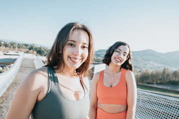 Portrait of two young sporty girls smiling to camera before starting to train. Working out clothes, top and leggings, African woman fitness. Sunset ambient, slim bodies.