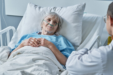 senior woman in oxygen tube in her nose lying on bed at the ward and having a treatment at hospital 