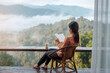 © Jo Panuwat D - young woman reading book near window and looking mountain view at countryside homestay in the morning sunrise. SoloTravel, journey, trip and relaxing concept