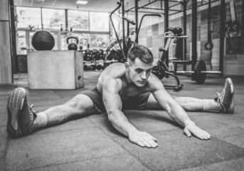 Wall Mural - Young muscular man practicing muscle stretching in modern health club