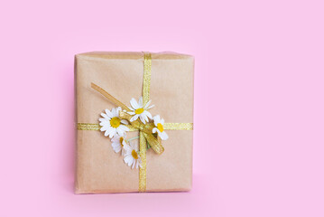 Sticker - Gift in a box tied with a golden ribbon and a bouquet of daisies on a pink pastel background. Gift for March 8 or Mother's Day.