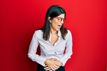 Wall Mural - Young hispanic woman wearing business shirt and glasses with hand on stomach because nausea, painful disease feeling unwell. ache concept.