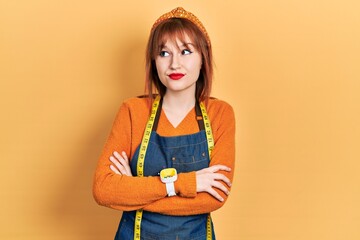 Canvas Print - Redhead young woman dressmaker designer wearing atelier apron smiling looking to the side and staring away thinking.