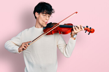 Poster - Handsome hipster young man playing violin making fish face with mouth and squinting eyes, crazy and comical.