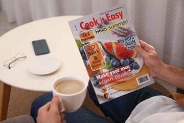 Poster - Man with cup of coffee reading magazine in armchair at home, closeup