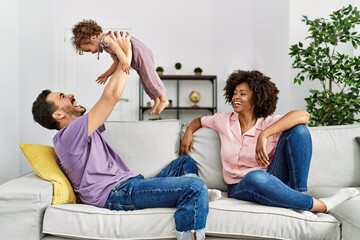 Canvas Print - Couple and daughter smiling confident holding child raised up at home