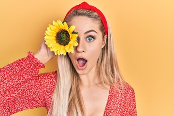 Poster - Young beautiful caucasian woman holding yellow sunflowers over eye scared and amazed with open mouth for surprise, disbelief face