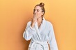 © Krakenimages.com - Young blonde woman wearing bathrobe bored yawning tired covering mouth with hand. restless and sleepiness.