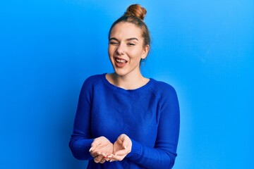 young blonde woman holding hands together cupped, giving concept winking looking at the camera with 