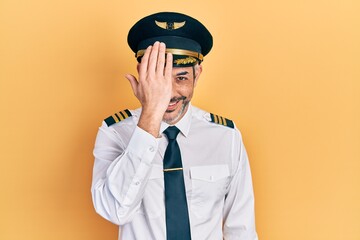 Poster - Handsome middle age man with grey hair wearing airplane pilot uniform covering one eye with hand, confident smile on face and surprise emotion.