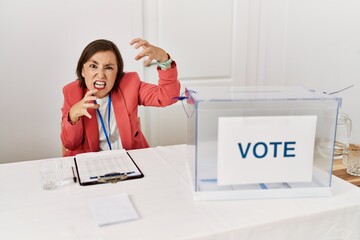 Canvas Print - Beautiful middle age hispanic woman at political election sitting by ballot shouting frustrated with rage, hands trying to strangle, yelling mad