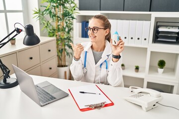 Canvas Print - Young doctor woman wearing uniform and stethoscope pointing thumb up to the side smiling happy with open mouth