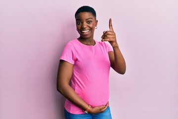 Sticker - Young african american woman expecting a baby, touching pregnant belly pointing finger up with successful idea. exited and happy. number one.