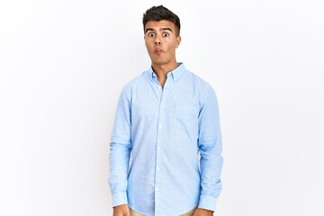 Poster - Young hispanic man wearing business shirt standing over isolated background making fish face with lips, crazy and comical gesture. funny expression.