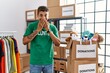 Young handsome hispanic man wearing volunteer t shirt at donations stand laughing and embarrassed giggle covering mouth with hands, gossip and scandal concept
