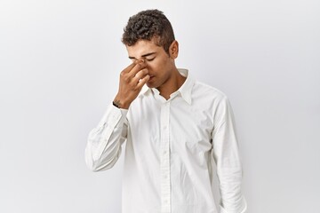 Poster - Young handsome hispanic man standing over isolated background tired rubbing nose and eyes feeling fatigue and headache. stress and frustration concept.