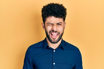 Sticker - Young arab man with beard wearing casual shirt winking looking at the camera with sexy expression, cheerful and happy face.