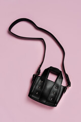 Wall Mural - Small leather black handbag on a pink background. Trendy accessories. Fashion concept. Flat lay, top view.