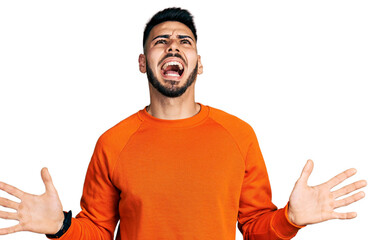 Wall Mural - Young hispanic man with beard wearing casual orange sweater crazy and mad shouting and yelling with aggressive expression and arms raised. frustration concept.