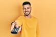 © Krakenimages.com - Young hispanic man with beard holding television remote control celebrating crazy and amazed for success with open eyes screaming excited.