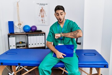 Sticker - Young physiotherapist man working at pain recovery clinic looking at the watch time worried, afraid of getting late