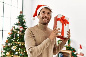 Young hispanic man smiling confident holding christmas gift at home