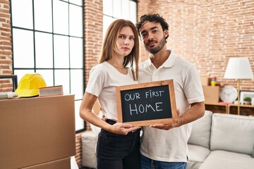 Canvas Print - Young two people holding blackboard with first home text relaxed with serious expression on face. simple and natural looking at the camera.