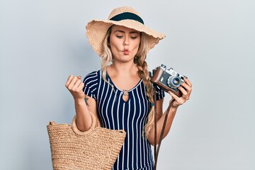 Sticker - Beautiful young blonde woman holding vintage camera making fish face with mouth and squinting eyes, crazy and comical.