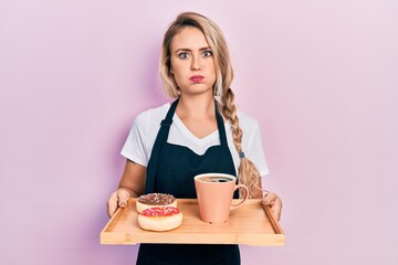 Wall Mural - Beautiful young blonde woman wearing waitress apron holding breakfast tray puffing cheeks with funny face. mouth inflated with air, catching air.