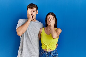 Sticker - Young hispanic couple standing together over blue background yawning tired covering half face, eye and mouth with hand. face hurts in pain.