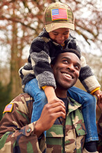 American Soldier In Uniform Returning Home To Family On Leave Carrying Son Wearing Army Cap
