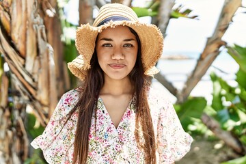 Poster - Young latin girl smiling happy wearing summer hat standing at the beach.