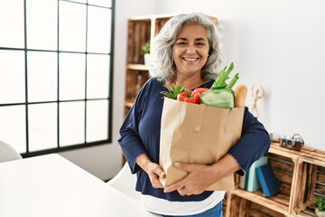 Sticker - Middle age grey-haired woman holding paper bag with groceries standing at home.