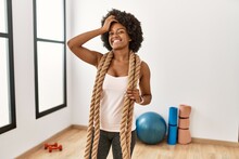 Young African American Woman With Afro Hair At The Gym Training With Battle Ropes Smiling Confident Touching Hair With Hand Up Gesture, Posing Attractive And Fashionable