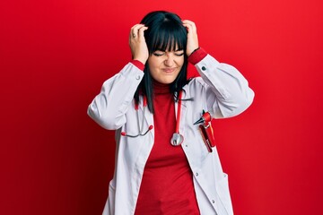 Poster - Young hispanic woman wearing doctor uniform and stethoscope suffering from headache desperate and stressed because pain and migraine. hands on head.