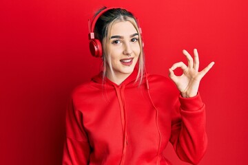 Sticker - Young modern girl wearing gym clothes and using headphones smiling positive doing ok sign with hand and fingers. successful expression.