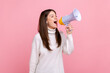© khosrork - Side view portrait of pretty positive girl screaming in megaphone, announcing important information, wearing white casual style sweater. Indoor studio shot isolated on pink background.