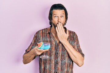 Poster - Middle age caucasian man drinking tropical cocktail with alcohol covering mouth with hand, shocked and afraid for mistake. surprised expression