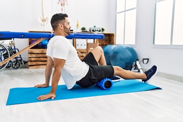 Canvas Print - Young hispanic man patient smiling confident having leg rehab session using foam roller at clinic