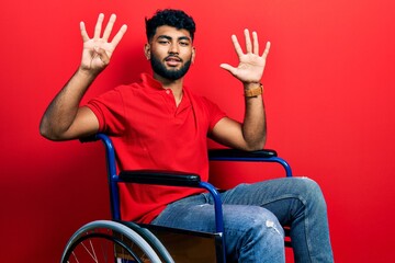 Canvas Print - Arab man with beard sitting on wheelchair showing and pointing up with fingers number nine while smiling confident and happy.