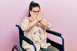 Young hispanic woman sitting on wheelchair rejection expression crossing arms doing negative sign, angry face