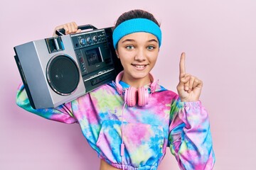 Sticker - Young brunette girl wearing workout clothes and holding boombox smiling with an idea or question pointing finger with happy face, number one