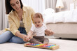 © New Africa - Cute baby and mother playing with xylophone on floor at home