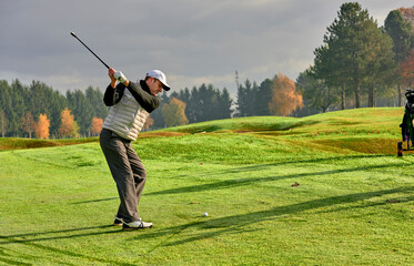 Wall Mural - Golfer on a golf course in winter with wet grass, hitting the ball with a golf club.