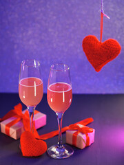 Canvas Print - Valentine's day romantic dinner. Two glasses of champagne, gift boxes and a red knitted heart symbol of love. Neon bokeh background