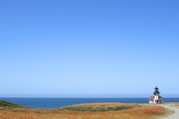 Wall Mural - Distant lighthouse station on a filed overlooking a blue ocean