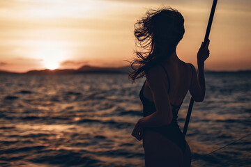 Wall Mural - Portrait of a wonderful and interesting girl posing on her boat. Silhouette of a girl in a bikini on a sunset background. Against the backdrop of the raging sea and nature on the horizon