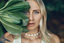 Portrait Of A Young Blond Woman With A Sharming Eyes Covering With Blue Liner And Holding Big Leaves Of Wild Tree. Close Up;. Vacation Concept.